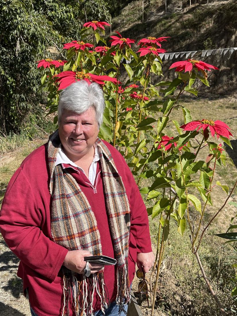 Dr. Nancy Strickland beside a poinsettia at The Happiness Farm, Paro